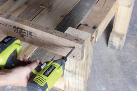 person using an electric drill on the side of a wooden chair